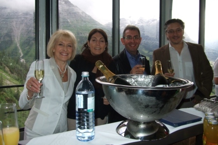 Four people in a cable car raising glasses of champagne with wine bucket and bottle of water in foreground