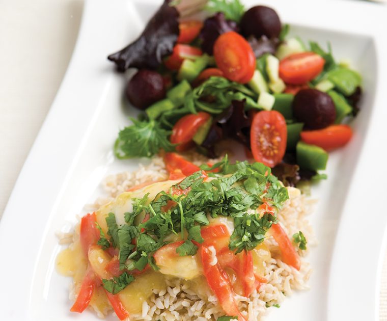 A rectangular plate of sweet chilli chicken on a bed of white rice with a mixed salad