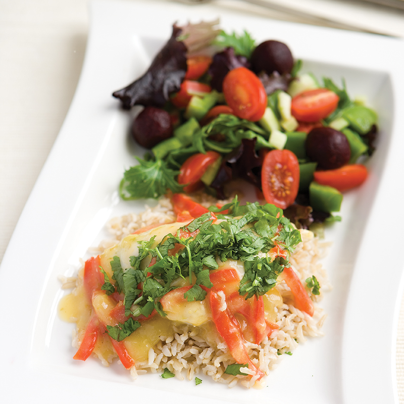 A rectangular plate of sweet chilli chicken on a bed of white rice with a mixed salad