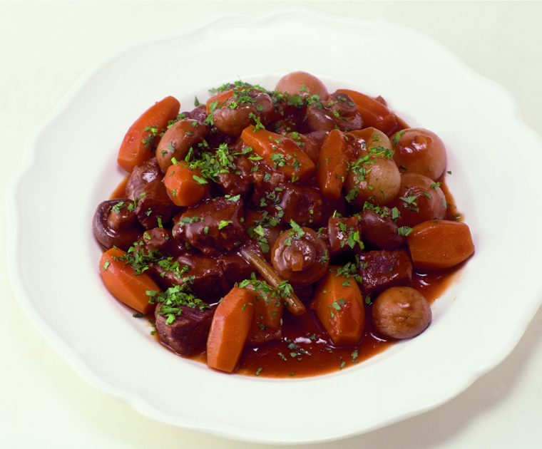 Plate of Beef Bouguignon with beef, carrots, mushrooms and celery in a tomato based gravy sprinkled with fresh thyme