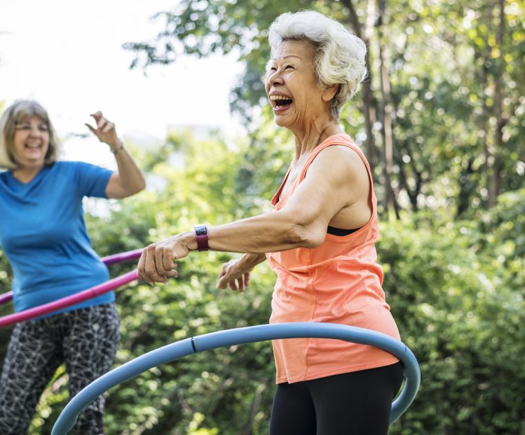 Two senior woman laughing exercising with a hula hoop