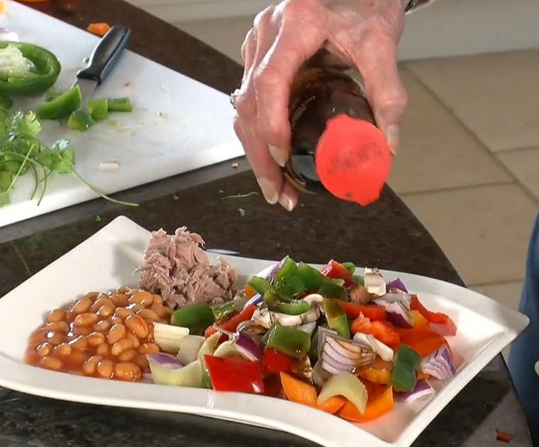 A hand sprinkling a bottle of balsamic vinigar over a plate of Crunchy Pepper Salad