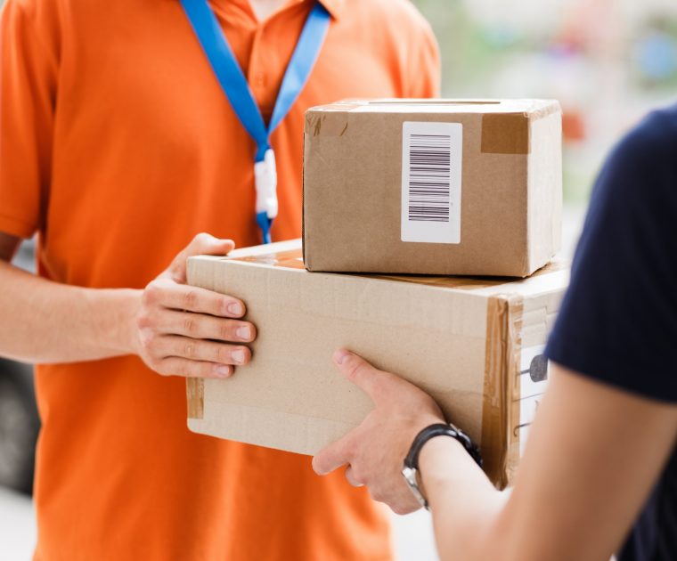 A person wearing an orange T-shirt and a name tag is delivering parcels to a client.