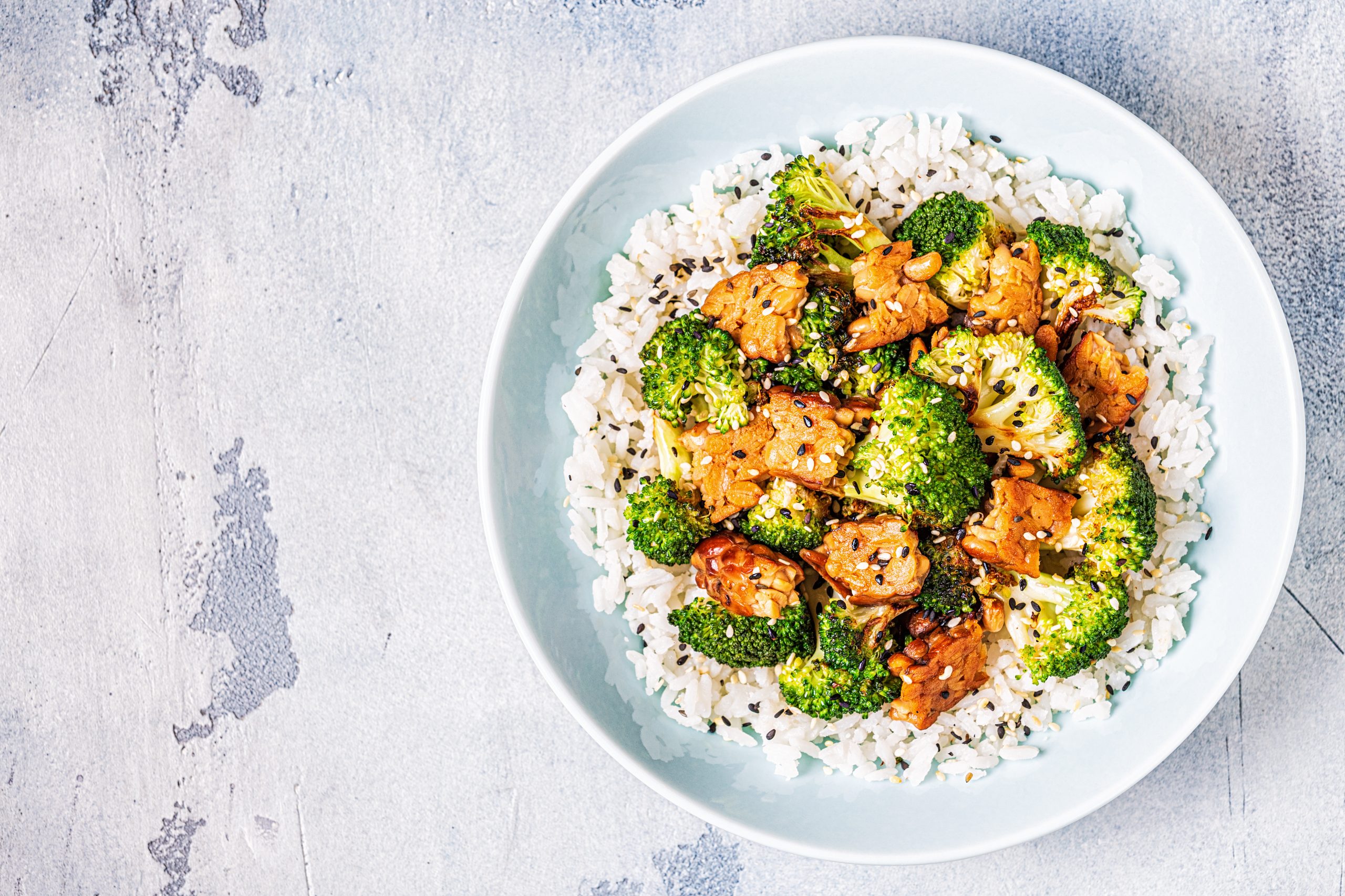 A round dish of fried tempeh and broccoli on a bed of white rice