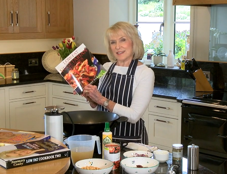 Rosemary Conley in her kitchen holding a copy of her Low Fat Vegetarian Recipes book