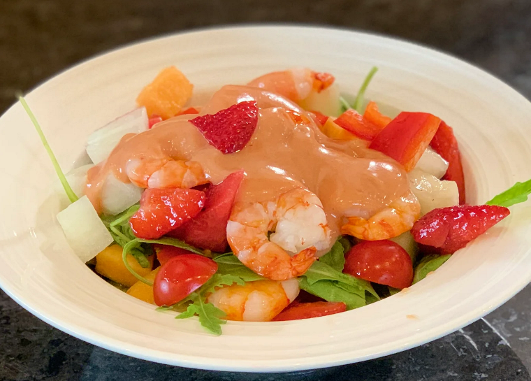 A bowl of Meditarranean Prawn Salad including prawns, strawberries, melon, tomatoes and salad leaves