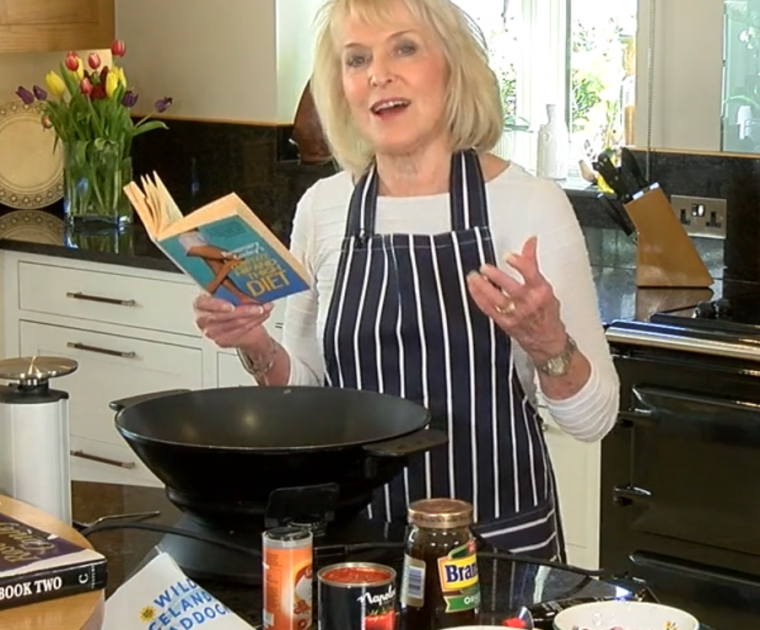 Rosemary Conley in the kitchen with an electric wok reading a recipe out of her Hip & Thigh Diet book