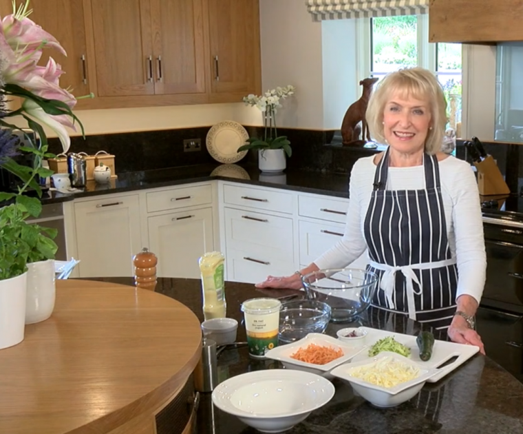 Rosemary Conley standing in her kitchen with salad ingredients on the worktop