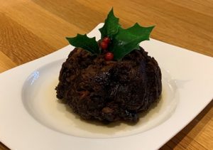 A low fat Christmas Pudding topped with holly sat on a white plate