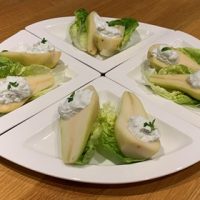 Four white quarter plates placed together to complete a circle with halved pears topped with Stilton cheese and Greek yoghurt on a bed of gem lettuce