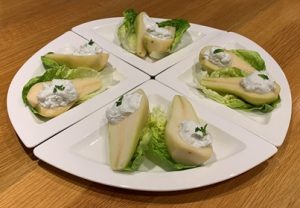 Four white quarter plates placed together to complete a circle with halved pears topped with Stilton cheese and Greek yoghurt on a bed of gem lettuce