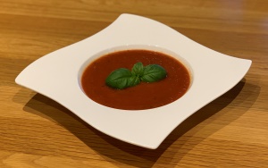 Easy Tomato & Roasted Garlic Soup in a white bowl decorated with a sprig of basil