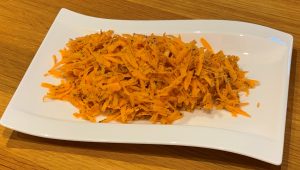 A sald of raw grated sweet potato on a rectangular white plate