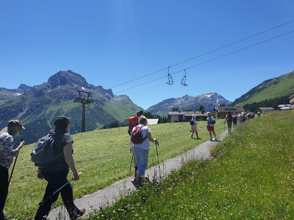 Austrian Activity Holiday group walking along a high mountain path through a grassy meadow passing under a closed ski-lift