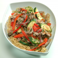 Thai Pork stir fry on a bed of noodles in a white bowl