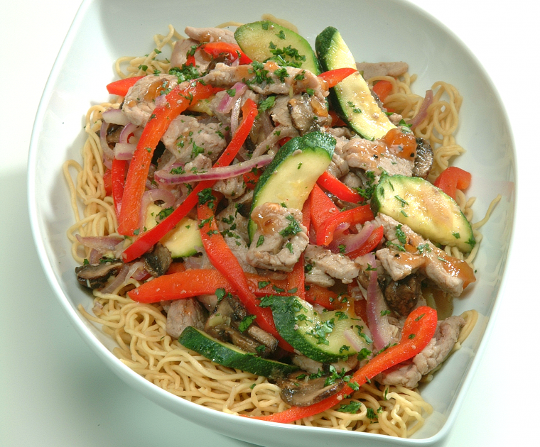 Thai Pork stir fry on a bed of noodles in a white bowl