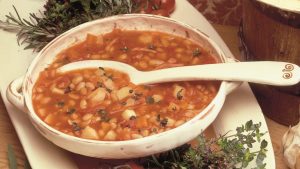 A hearty soup with bacon, white beans, pasta, garlic and herbs served in a large white bowl