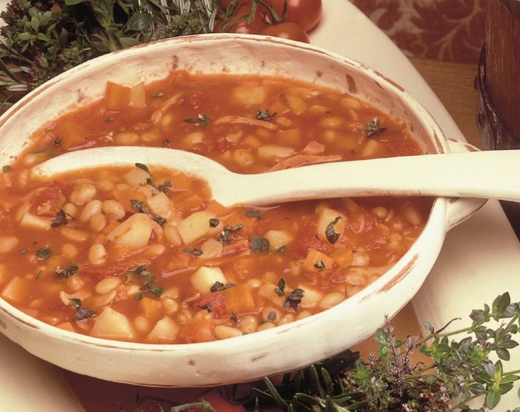 A hearty soup with bacon, white beans, pasta, garlic and herbs served in a large white bowl