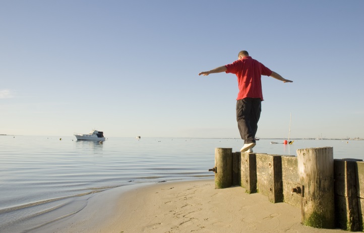 A man balancing along a small wooden sea-break barrier, on a beautiful and calm beach.