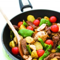 Slices of rump steak being stir-fried in a pan with onions, garlic, mushrroms, tomatoes and potatoes.