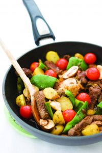 Slices of rump steak being stir-fried in a pan with onions, garlic, mushrroms, tomatoes and potatoes.