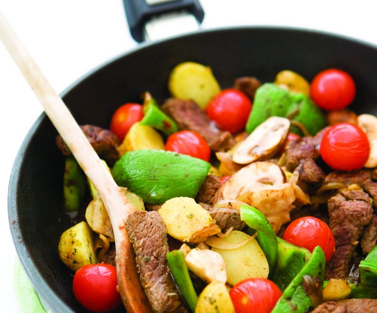 Slices of rump steak being stir-fried in a pan with onions, garlic, mushrroms, tomatoes and potatoes.