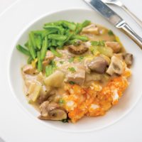 A creamy looking Pork and Leek Casserole on a white plate served with sweet potato mash and sliced green beans
