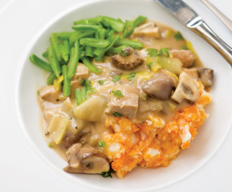 A creamy looking Pork and Leek Casserole on a white plate served with sweet potato mash and sliced green beans