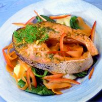 Baked salmon with ginger. A glazed baked salmon steak complete with skin on a bed of salad leaves sprinkled with ginger and dill