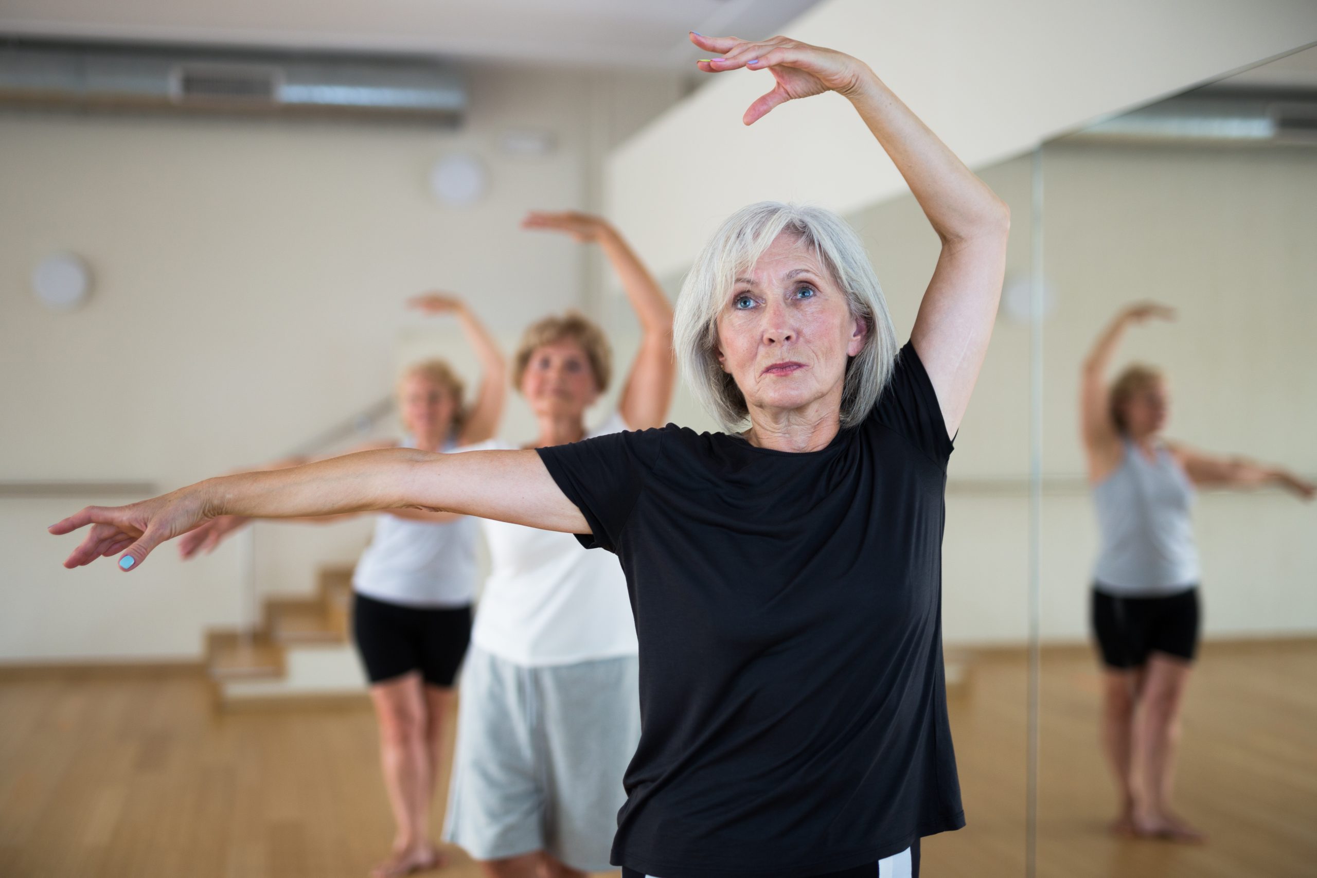 Portrait of a mature woman standing in the 3rd position of the ballet stand near the mirror at a group lesson in a dance studio
