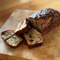 Banana and Sultana loaf cake on a cutting board with a couple of pieces sliced revealing the moist banana sponge and juicy sultanas.