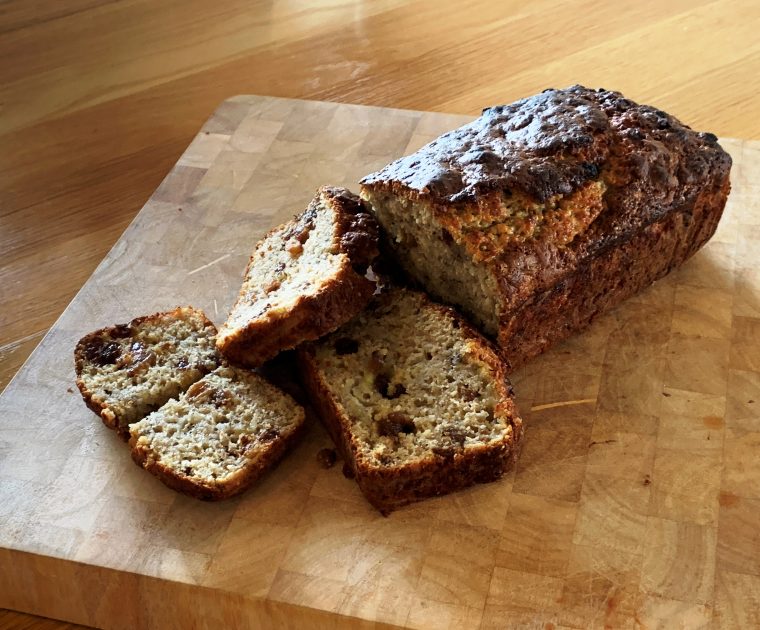 Banana and Sultana loaf cake on a cutting board with a couple of pieces sliced revealing the moist banana sponge and juicy sultanas.