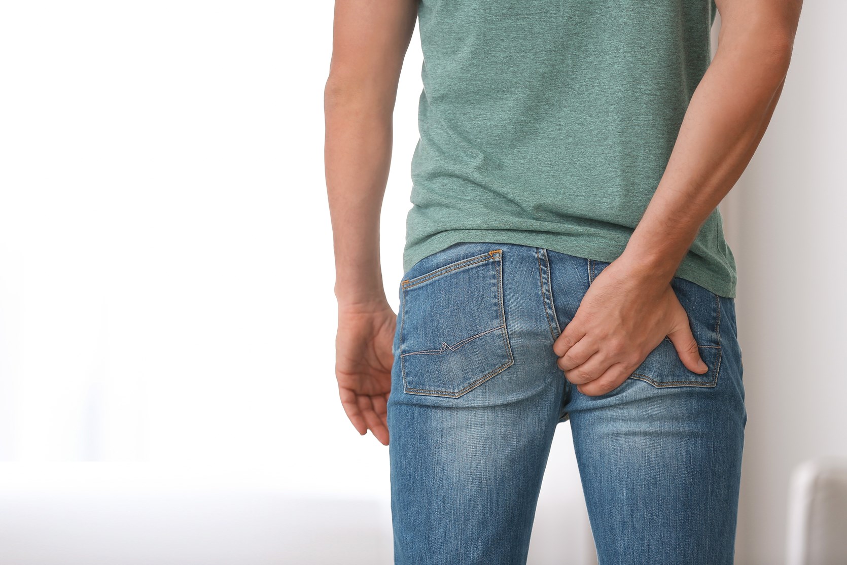Man dressed in blue denim jeans suffering from haemerrhiods scratches his bottom