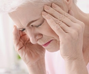 Senior woman illustrating a mental health issue by closing her eyes and touching her temples