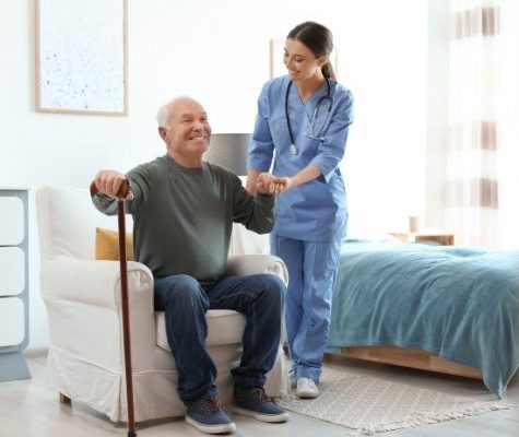 Care worker helping elderly man with stick in geriatric hospice