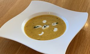 Butternut Squash and Thyme Soup in a white bowl garnished with pools of natural yogurt and a sprif of thyme