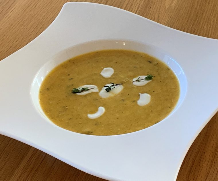 Butternut Squash and Thyme Soup in a white bowl garnished with pools of natural yogurt and a sprif of thyme