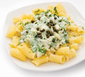 A dish of rigatoni pasta topped with a mixture of crushed broad beans, greek yogurt, capers, mint, chives and parsley