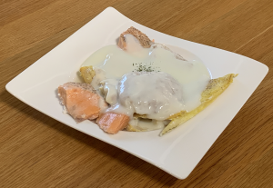 A medley of fresh cod, smoked haddock and salmon arranged on a white plate smothered in a white sauce.