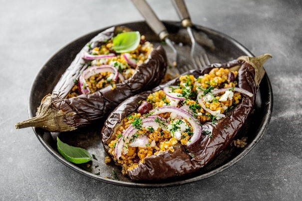 A plate with two baked aubergines stuffed with chickpeas, bulgar and a feta-style cheese.
