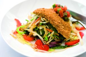 A crispy breadcrumbed fillet of chicken resting on top of a plate of stir-fried vegetables.