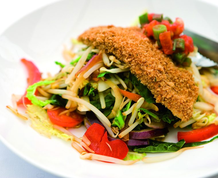 A crispy breadcrumbed fillet of chicken resting on top of a plate of stir-fried vegetables.