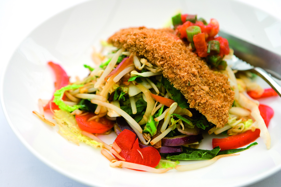 A crispy breadcrumbed fillet of chicken resting on top of a plate of stir-fried vegetables.
