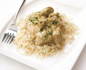 Chicken Korma on a bed of white rice is chunks of tender chicken in a creamy looking sauce sprinkled with finely chopped corriander