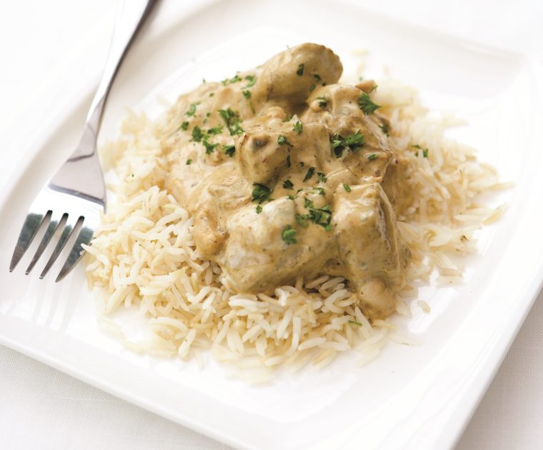 Chicken Korma on a bed of white rice is chunks of tender chicken in a creamy looking sauce sprinkled with finely chopped corriander.