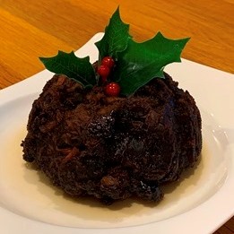 A low fat Christmas Pudding topped with holly sat on a white plate